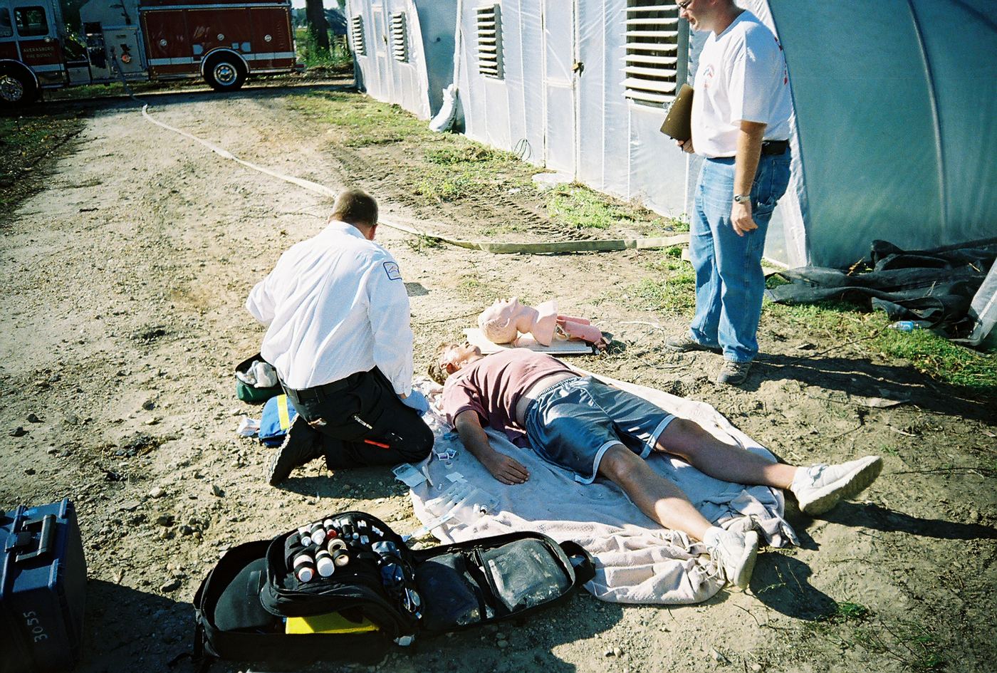 A medic kneeling beside a patient near white tents in Dunn, 2007